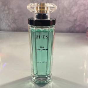 Säljer en elegant Eau de Parfum från BI-ES med namnet Eau Turquoise. Flaskan är stilren och har en turkos färg som ger en fräsch känsla. Den har en unik, facetterad kork som ger en lyxig touch. Perfekt för dig som vill ha en fräsch och uppfriskande doft i din samling.