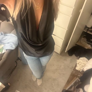 Svart ärmlös topp - Snygg svart ärmlös silkes topp nyskick med djup v-ringning och draperad framsida. Perfekt för en utekväll eller fest. Toppen har en elegant och stilren design som passar till både jeans och kjol.