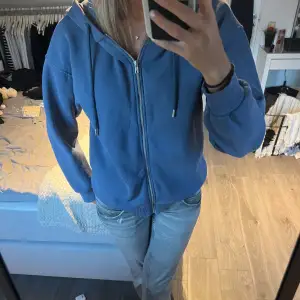 Säljer en snygg blå hoodie från Gina Tricot i storlek XS. Den har en dragkedja framtill och en skön huva med dragsko. Perfekt för en avslappnad stil och passar bra till jeans. Använd ett fåtal gånger, så den är i bra skick. Perfekt för höst och vår!