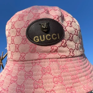 Gucci hatt i rosa och svart -  Gucci hat till salu! Den första är rosa med mönster och ett brunt lädermärke med Gucci-loggan. Den andra är svart med en enkel vit Gucci-brodering. Perfekta för att lyfta vilken outfit som helst!                                                         Kom med prisförslag!!!!!