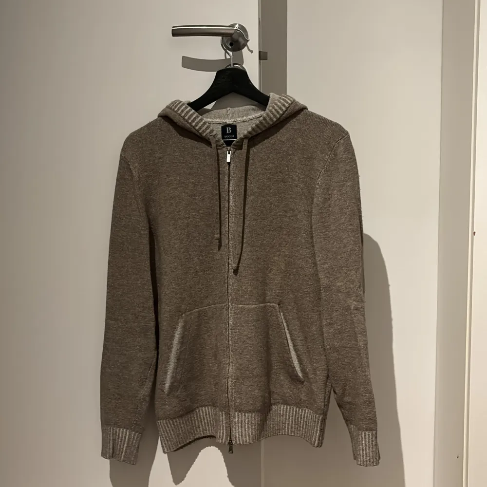 Säljer en supermjuk beige hoodie från Boggi i kashmirblandning. Perfekt för kyliga dagar med dragkedja och ribbade muddar. Den har en klassisk design med fickor fram och en bekväm passform. Perfekt för både vardag och avslappnade tillfällen. Og pris 2700kr. Tröjor & Koftor.