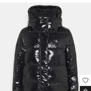 Svart pufferjacka från Calvin Klein - Snygg och glansig svart pufferjacka från Calvin Klein. Perfekt för kalla dagar med sin varma vaddering och stora huva. Jackan har en diskret CK-logga på bröstet och stängs med dragkedja. Den är långärmad och har en modern look. Skulle säga att jackan är liten i storlek. Använd väldigt sparsamt därav i väldigt bra skick. Kommer inte sälja under 1300 då nypriset var ungefär 2200.☺️