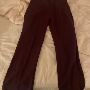 Vinröda kostym byxor - Säljer ett par vinröda byxor i bra skick. De har en elegant och stilren design, perfekt för både vardag och fest. Byxorna har en rak passform och är tillverkade i ett mjukt material som ger en bekväm känsla hela dagen.