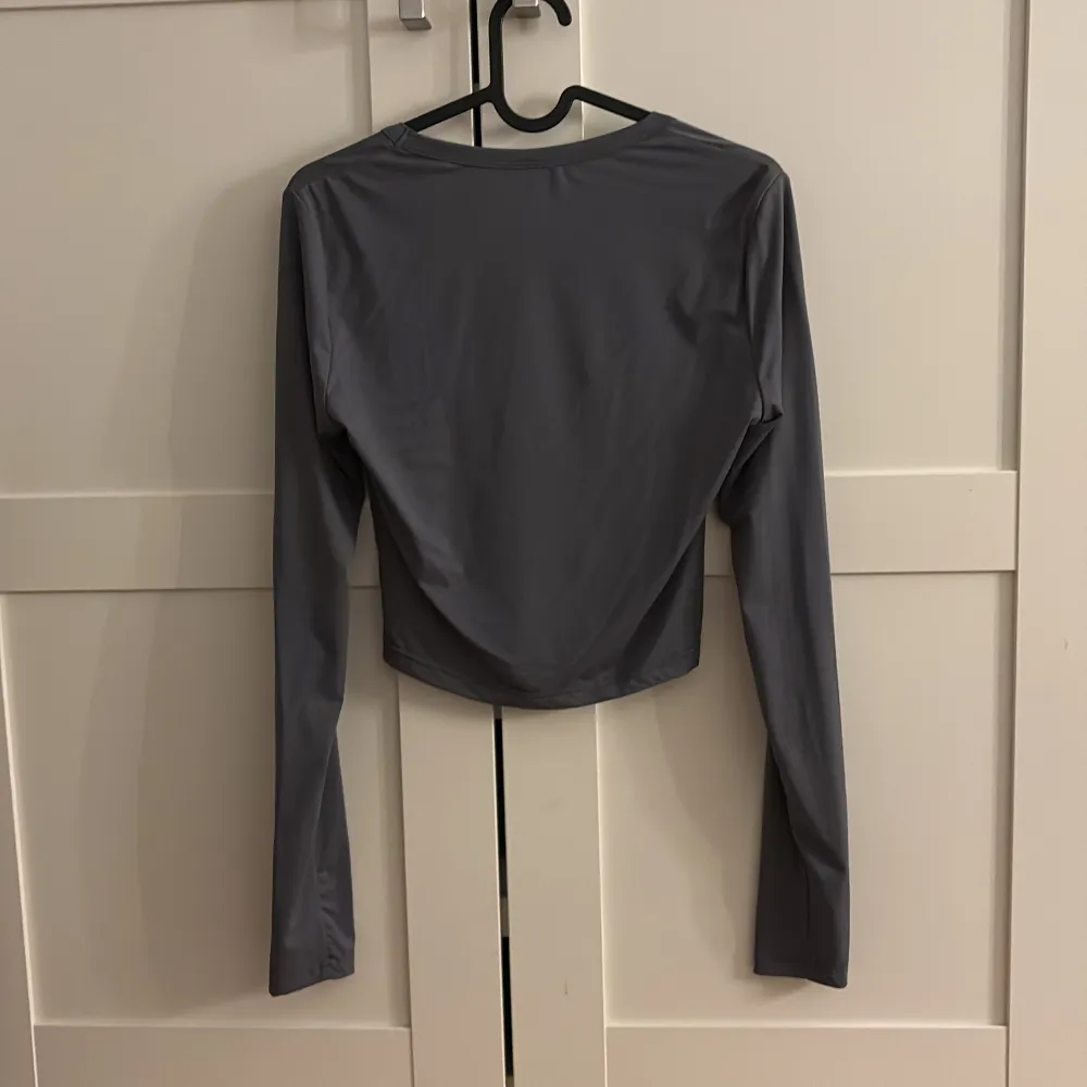 Snygg grå långärmad topp i syntetmaterial. Den har en rundad halsringning och är croppad, vilket ger en modern look. Perfekt för både vardag och festliga tillfällen. Toppen är i mycket bra skick och passar perfekt till jeans eller kjol.. Neuletakit & Villapaidat.