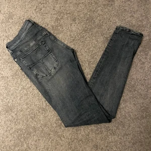 Grå jeans från Tiger of Sweden - Säljer ett par snygga grå jeans från Tiger of Sweden i slim fit. De är tillverkade i Italien och har en klassisk design med fem fickor och knappgylf 