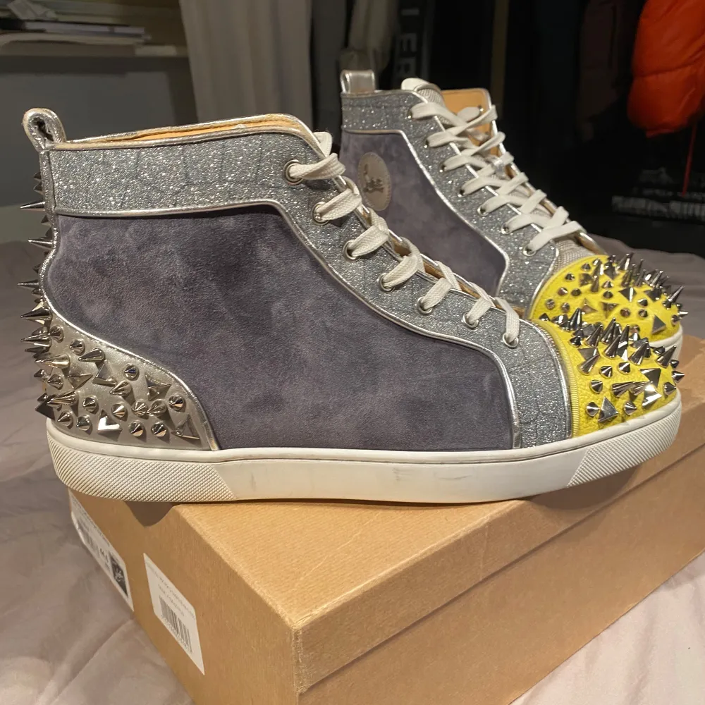 Lämna pris förslag! Säljer ett par unika sneakers från Christian Louboutin i grå mocka med glittriga detaljer och gula tår. Skorna har coola nitar runtom och den klassiska röda sulan. Perfekta för att sticka ut på festen! De är i mycket bra skick och har snörning för bästa passform. Skicket på skorna är 8/10😊. Skor.