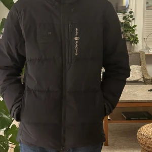 Svart dunjacka från Sail Racing - Säljer en svart dunjacka från Sail Racing i storlek S. Jackan är i mycket bra skick och perfekt för kalla vinterdagar. Den har en dragkedja framtill och är långärmad. Materialet är vindtätt och andas bra, vilket gör den idealisk för utomhusaktiviteter. Den är också fluorkarbonfri och DWR-behandlad för extra skydd mot väder och vind.