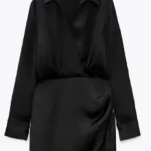 Svart omlottklänning - Snygg svart omlottklänning i satin med långa ärmar och en elegant v-ringning. Perfekt för festliga tillfällen med sin stilrena design och fina drapering. Klänningen har en kort längd som ger en modern och chic look.