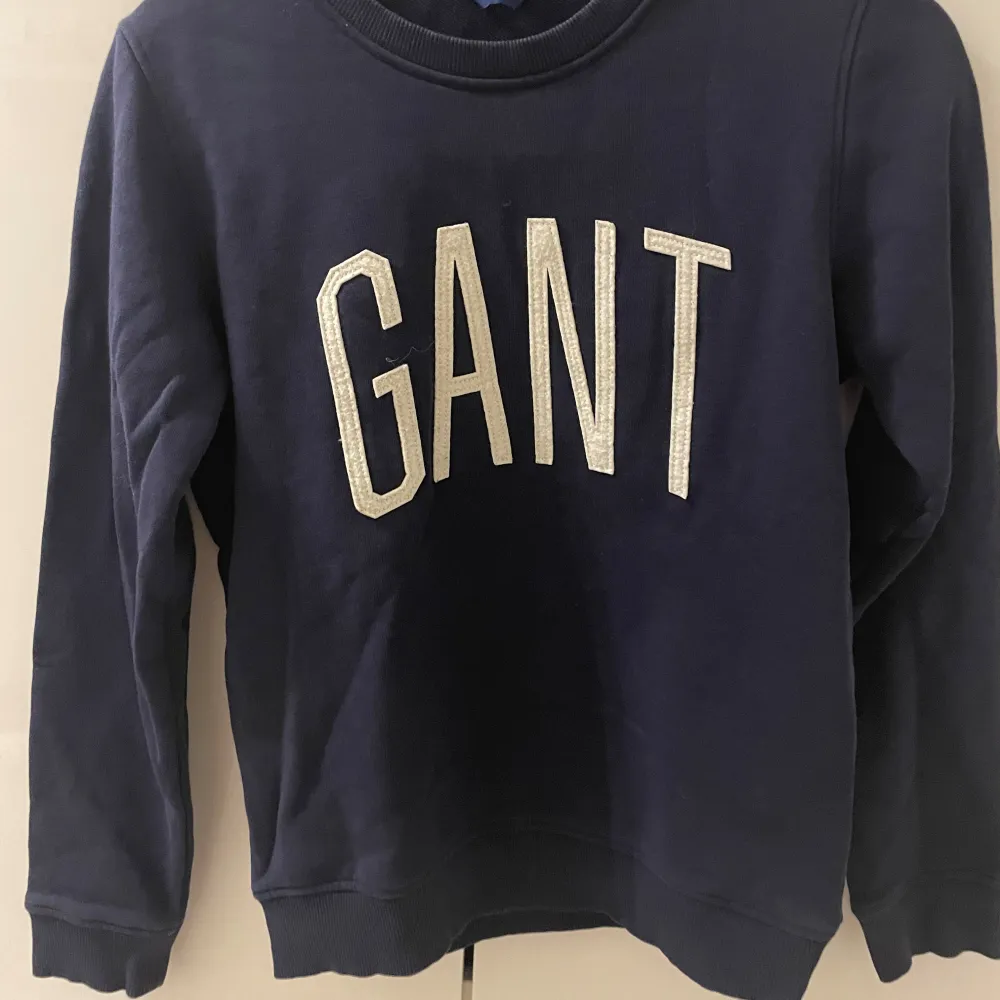 Säljer en snygg mörkblå sweatshirt från GANT i storlek XS. Tröjan har ett stort GANT-tryck i vitt på framsidan och är i mycket bra skick. Perfekt för höst och vinter, med långa ärmar och mjukt material. Har inget slitage❄️💙. Tröjor & Koftor.