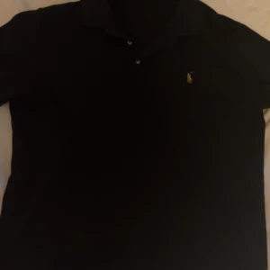 Svart pikétröja från Ralph Lauren - Säljer en stilren svart pikétröja från Ralph Lauren i storlek L. Tröjan har en klassisk krage och är i slim fit-modell. Den är prydd med det ikoniska broderade logotypen på bröstet. Perfekt för både vardag och fest!