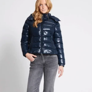 Mörkblå pufferjacka med huva - Säljer denna eftertraktade mörkblåa pufferjackab med glansig finish. Jackan har en praktisk huva och dragkedja framtill. Perfekt för kyliga dagar och håller dig varm och stilren. Passar bra till både vardag och utflykter. storlek M men passarig som brukar bära xs/s, helt ny!