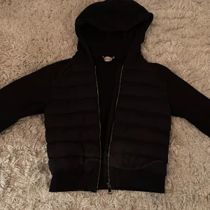 Svart jacka med huva från Moncler - Säljer en snygg svart jacka från Moncler i mycket bra skick. Den har en huva och dragkedja framtill. 
