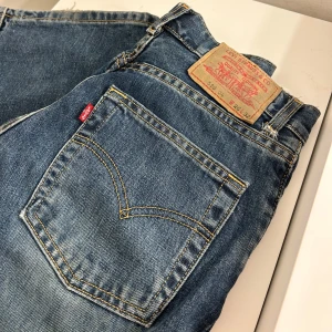 Levis 501 jeans - Säljer ett par klassiska Levis 501 jeans i blå denim. De är i bra skick med den ikoniska femficksdesignen och knappgylf. Perfekta för en avslappnad stil och passar till det mesta. Storleken är inte angiven, men de ser ut att vara i en standard passform. Skulle säga att dem passar 32. 