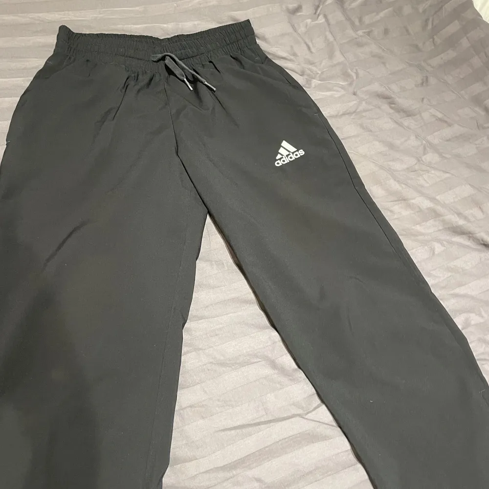 Säljer ett par svarta träningsbyxor från Adidas i storlek S. Byxorna har en elastisk midja med snörning och är tillverkade av Primegreen-material. De har en dragkedja vid bensluten för extra komfort. Perfekta för träning eller en avslappnad dag.. Farkut & Housut.