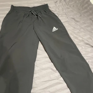 Svarta träningsbyxor från Adidas - Säljer ett par svarta träningsbyxor från Adidas i storlek S. Byxorna har en elastisk midja med snörning och är tillverkade av Primegreen-material. De har en dragkedja vid bensluten för extra komfort. Perfekta för träning eller en avslappnad dag.