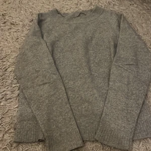 Grå stickad tröja  - Mysig grå stickad tröja från Vero Moda i storlek S. Perfekt för kyliga dagar med sin mjuka och bekväma passform. Tröjan har långa ärmar och ribbade detaljer vid hals och ärmslut. Ett måste för höst- och vintergarderoben!
