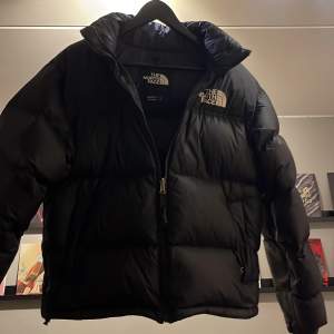 Säljer en svart dunjacka från The North Face i mycket bra skick. Jackan har en pufferstil med dragkedja och är perfekt för kalla vinterdagar. Den är märkt med '700', vilket indikerar hög kvalitet och värmeisolering. Perfekt för dig som vill hålla dig varm och snygg i vinter! Den är i toppenskick utan några synliga skador! PRISET ÄR JUSTERBART VID SNABB AFFÄR!