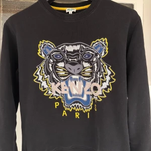 Kenzo tröja - Säljer en svart tröja från Kenzo med ett stort, färgglatt tigerbroderi på framsidan. Tröjan har långa ärmar och är perfekt för både vardag och fest. Den är i bra skick och redo för en ny ägare! Obs: skriv innan köp!