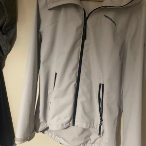 Vit vindjacka från Peak Performance - Säljer en snygg vit vindjacka från Peak Performance. Jackan har en dragkedja framtill och praktiska fickor med dragkedjor. Perfekt för vår och höst med sin lätta och funktionella design. Den har en huva för extra skydd mot väder och vind. Den är mindre i storlek så den passar L.