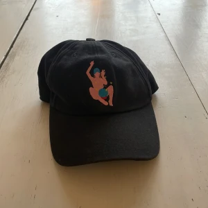 Svart keps från Carne bollente - Säljer en svart keps med broderad design framtill. Kepsen har en justerbar rem baktill. Den är oanvänd och från ett Parisiskt märke. 