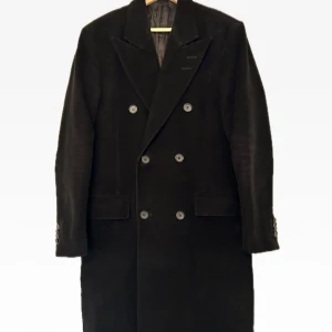 Svart rock/kappa från Tiger of Sweden - Säljer en elegant svart kappa från Tiger of Sweden i mycket bra skick. Den har en klassisk dubbelknäppt design med knappar och långa ärmar. Perfekt för höst och vinter, och ger en stilren look. Passar både till vardags och festliga tillfällen.