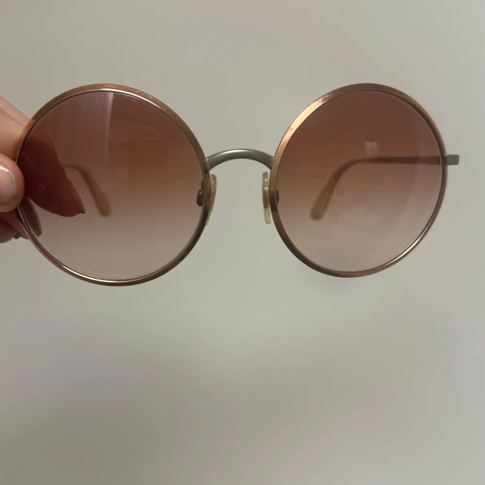 Säljer ett par snygga runda solglasögon från Dolce & Gabbana. De har en tunn guldfärgad metallram och bruna tonade glas. Perfekta för en stilren look i sommar! Kommer med originalfodral.. Accessoarer.