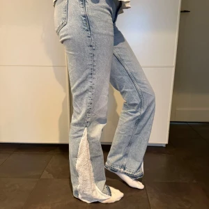 Ljusblå jeans med vita detaljer - Säljer ett par ljusblå jeans med unika vita slitsdetaljer längs benen. De har en bootcut-stil som ger en snygg siluett och är perfekta för både vardag och fest. Jeansen är i bra skick och har en klassisk femficksdesign. Perfekta för dig som vill ha något lite annorlunda i garderoben! 💙 Midja: 35 cm innerbenslängd: 79 cm ytterbenslängd: 103 cm