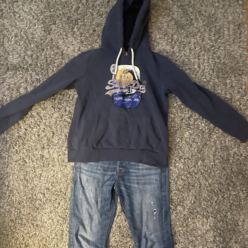 Säljer en snygg mörkblå hoodie från Superdry med coolt tryck på framsidan. Den har en klassisk känguruficka och justerbar huva med vita snören. Perfekt för en avslappnad stil och passar bra till jeans. Hör av dig om du är intresserad! 💙 Nypris 1500. Hoodies.