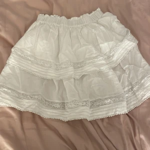 Vit kjol från BikBok - Säljer en superfin vit kjol från BikBok i storlek XS. Köpt för 400 kr och aldrig använd. Kjolen har volanger och spetsdetaljer som ger en extra detalj. Perfekt för sommardagar eller en söt festlook. Resår i midjan för en bekväm passform. Den är ganska stor i storleken så passar strl S och M💗