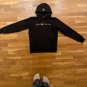 Svart hoodie från Sail Racing - Säljer en svart hoodie från Sail Racing i bra skick. Den har en klassisk design med logga på bröstet och en stor ficka framtill. Perfekt för höst och vinter, och den är superbekväm att ha på sig. Passar både till vardags och chillkvällar. 