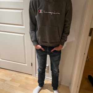 Grå hoodie från Champion - Säljer en snygg grå hoodie från Champion i bra skick. Den har en stor logga på bröstet och en praktisk magficka. Perfekt för höst och vinter, och den är superbekväm att ha på sig. Passar till både jeans och mjukisbyxor!