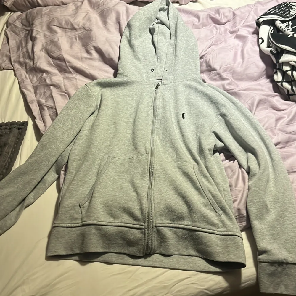 Säljer en snygg och bekväm grå hoodie från Polo Ralph Lauren. Den har en klassisk design med dragkedja och den ikoniska loggan broderad på bröstet. Perfekt för både vardag och chill. Passar bra till jeans eller joggers!. Tröjor & Koftor.