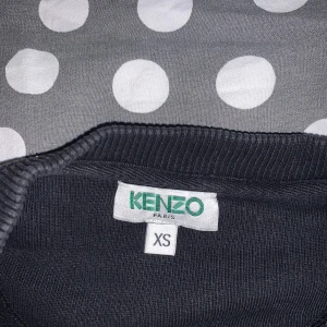 Svart tröja från Kenzo - Säljer en snygg svart tröja från Kenzo i storlek XS. Tröjan har ett stort Kenzo Paris-tryck i vitt och turkost på framsidan. Perfekt för både vardag och fest! 🖤