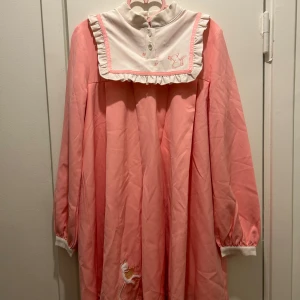 Kawaii klänning  - Söt rosa klänning med lång ärm och vit krage. Den har en gullig broderad kattdetalj framtill och knappar i nacken. Finns viss slitage på klänningen. 