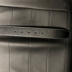 Svart skärp med silverfärgat spänne - Säljer ett stilrent svart skärp i skinn med ett stort silverfärgat H-spänne. Perfekt för att ge en elegant touch till vilken outfit som helst. Skärpet har en texturerad yta och flera hål för justering. Passar både till vardags och fest!