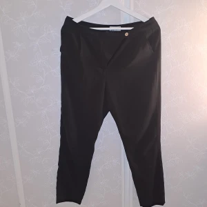 Svarta kostymbyxor  - Säljer ett par stilrena svarta kostymbyxor från Gina Tricot i storlek 38. De har en enkel design med knappdetalj och är perfekta för både vardag och fest. Byxorna är i bra skick och har en normal passform. Perfekta för höst och vår!✨️