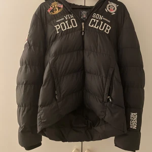Svart pufferjacka från Vinson Polo Club Storlek 170 kostade 1700kr - Säljer en svart pufferjacka från Vinson Polo Club i mycket bra skick helt oanvänd. Jackan har broderade detaljer och en dragkedja framtill. Perfekt för höst och vinter med sin varma och quiltade design. Den har en huva med text och är långärmad. Passar både till vardags och lite finare tillfällen.