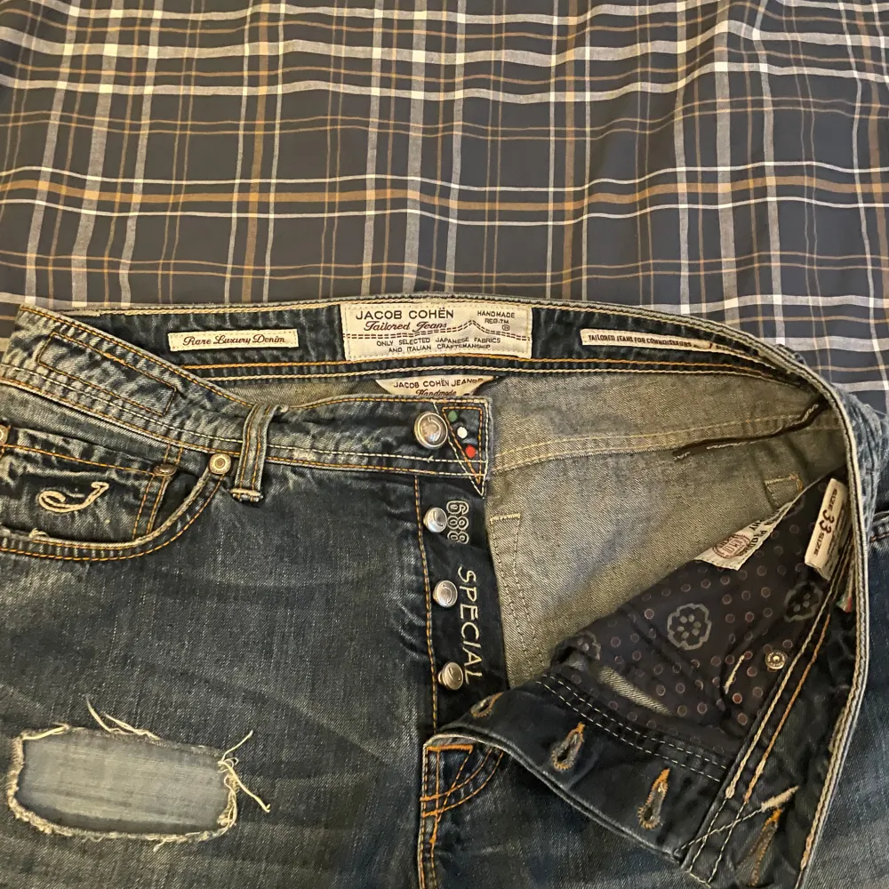 Säljer ett par snygga blå/grå jeans från Jacob Cohen i storlek 33. De har en cool slitning på framsidan och knappar istället för dragkedja. Perfekta för en avslappnad stil. Passar bra till både vardag och fest!. Jeans & Byxor.