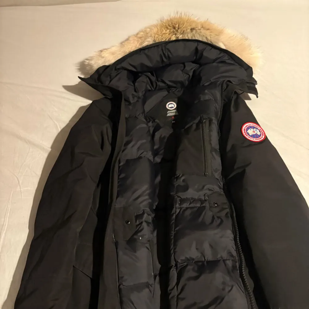 Säljer en svart dunjacka från Canada Goose i mycket bra skick. Jackan har en fluffig pälsdetalj på huvan och är perfekt för kalla vinterdagar. Den har en dragkedja framtill och flera praktiska fickor. Supervarm och stilren!. Jackor.