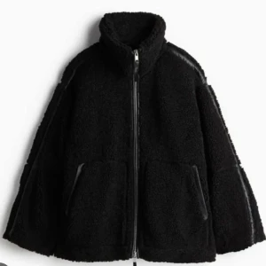 Svart teddyjacka med dragkedja - Mysig svart teddyjacka perfekt för kyliga dagar. Den har en dragkedja framtill och långa ärmar. Jackan är i ett oversized snitt vilket gör den extra bekväm och trendig. Perfekt för höst och vinter!