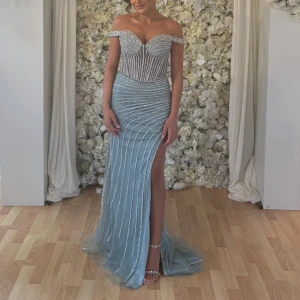 Ljusblå glittrig långklänning - Säljer en fantastisk ljusblå långklänning med glittriga detaljer. Klänningen har en elegant offshoulder-design och en smickrande slits framtill. Perfekt för bal eller fest! ✨
