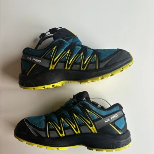 Salomon XA Pro löparskor - Säljer ett par Salomon XA Pro löparskor i blått och svart med gula detaljer. Skorna har en robust design med snörning och en slitstark sula perfekt för terränglöpning. De är i bra skick och redo för nya äventyr!