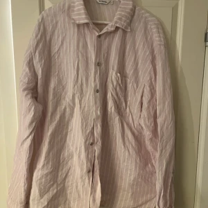 Rosa och vit randig skjorta från Marimekko - Säljer en superfin rosa och vit randig skjorta från Marimekko. Den har en klassisk krage och knappar framtill. Skjortan är långärmad och har en bröstficka. Perfekt för både vardag och lite mer uppklädda tillfällen. Materialet känns skönt och luftigt, perfekt för vår och sommar!