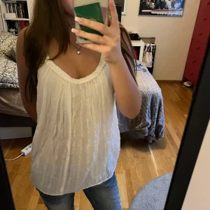 Vit ärmlös topp - Säljer en superfin vit ärmlös topp med en avslappnad passform. Den har en snygg, flätad kant vid halsringningen. Materialet är lätt och luftigt.