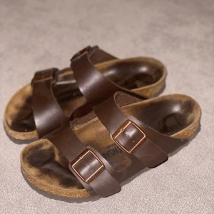 Birkenstock Arizona  - Birkenstock Arizona  Storlek: 36 Färg: Mörkbrun Skick: sparsamt använda, fint skick Nypris: 995:-