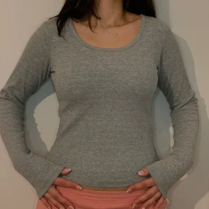 Grå ribbad långärmad topp - Säljer en stilren grå ribbad topp med långa ärmar. Perfekt för en avslappnad look. Passar bra till både jeans och kjol.