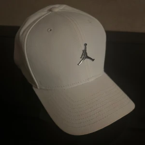 Vit Jordan keps  - Snygg vit keps med en stilren logotyp framtill. Kepsen har justerbar rem baktill för perfekt passform. Perfekt för en sportig look eller vardagsstil.