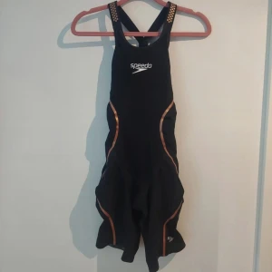 Tävlingsbaddräkt speedo - En svart tävlingsbaddräkt med guld detaljer från Speedo   Stl: 25  Orginal pris: 4 100kr  Köptes i december 2022 och använd under lite över ett år, säljer på grund av att jag slutat simtävla. Den är i bra skick utan skador, se bilder.  Jag är 173 cm lång, väger 55 kg och det tar ca 12 min för mig att ta på mig baddräkten. Den är svårast att få över höfterna för mig resten går på relativt enkelt.