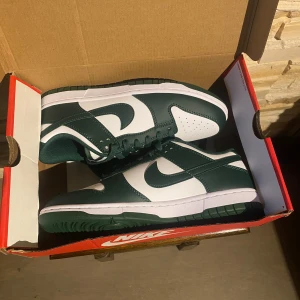 Nike Dunk Low Michigan State - Helt nya Nike Dunk Low Michigan State i storlek 42,5 EU säljes. Skorna har en stilren design i grön och vit läderfinish, vilket gör dem både klassiska och mångsidiga. Perfekta för sneakersamlaren eller som en statement-pjäs i din garderob. Aldrig använda och i originalskick, inklusive kartong. En eftertraktad modell för både fans av Nike och streetwear-entusiaster. Kontakta för fler bilder eller frågor!”