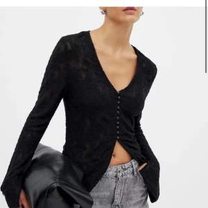 Svart långärmad topp med knappar - Snygg svart långärmad topp med v-ringning och knappar framtill. Perfekt för en stilren look. Passar bra till jeans eller kjol.